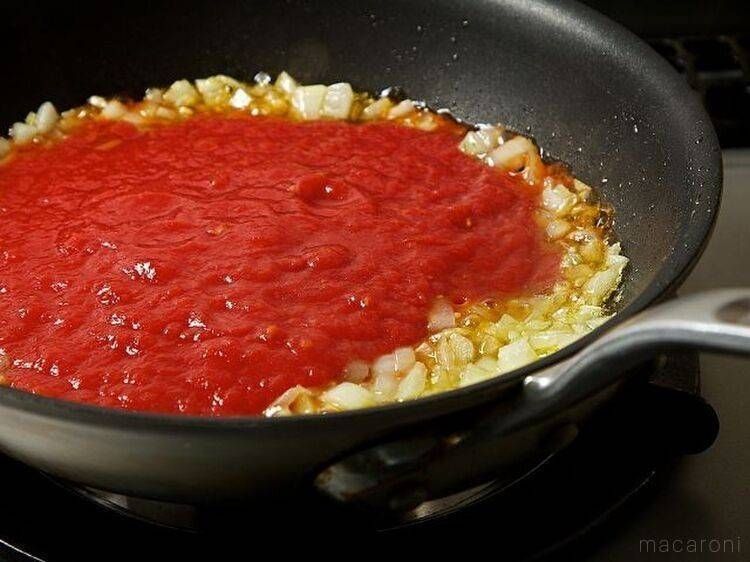 玉ねぎとにんにくを炒めた黒いフライパンに、トマトピューレを加えた様子