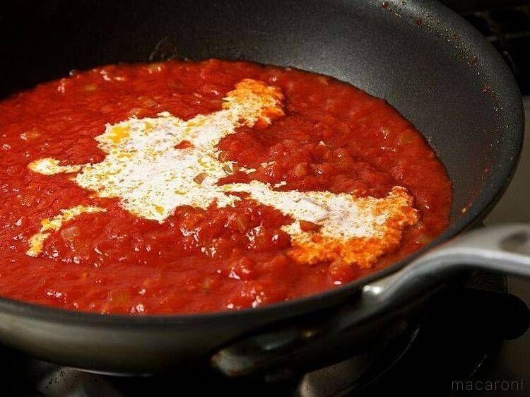 黒いフライパンに入ったトマトソースに、生クリームを加えた様子