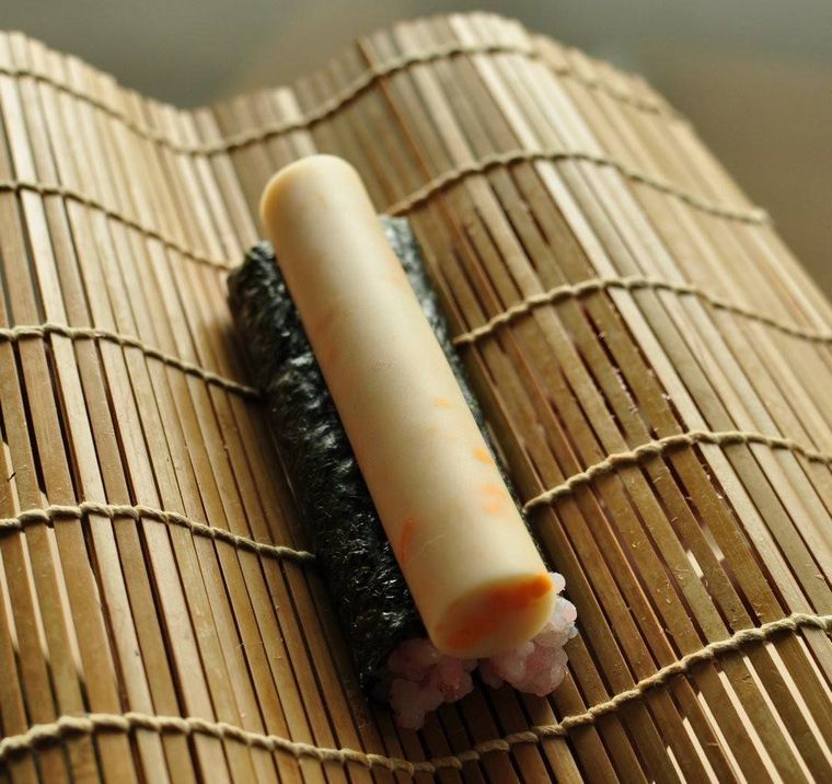 巻きすの上に置かれた細い海苔巻き2本とチーズ入りかまぼこ