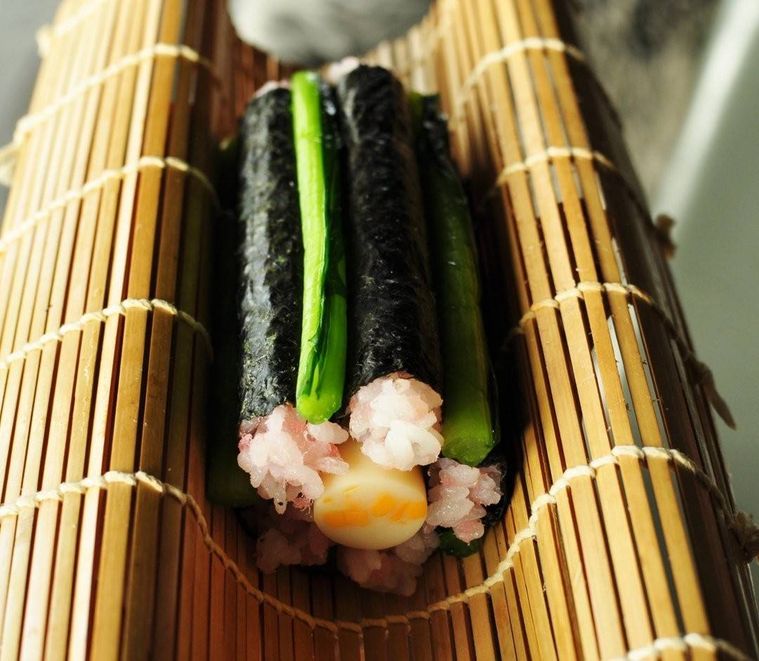 巻きすの上に置かれた細い海苔巻きとチーズ入りかまぼこと野沢菜漬け