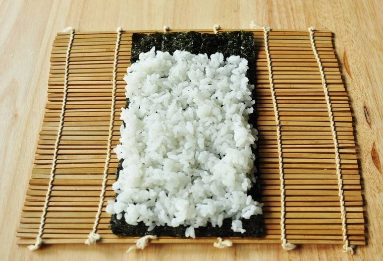 巻きすの上に置かれた海苔の上に白い寿司飯が広げられている