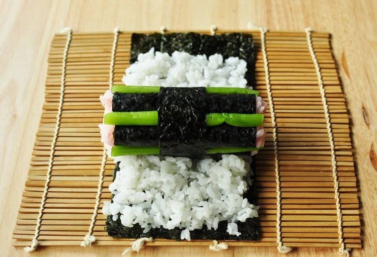 広げた海苔と寿司飯の上に細い海苔巻きの束がのせられている