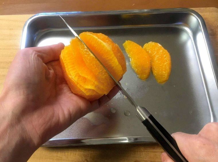 包丁を薄皮にそって入れて、オレンジの実を切り分けている様子