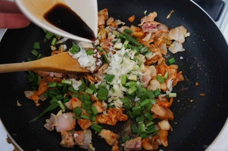 黒いフライパンで炒めた具材に、調味料を加えている様子