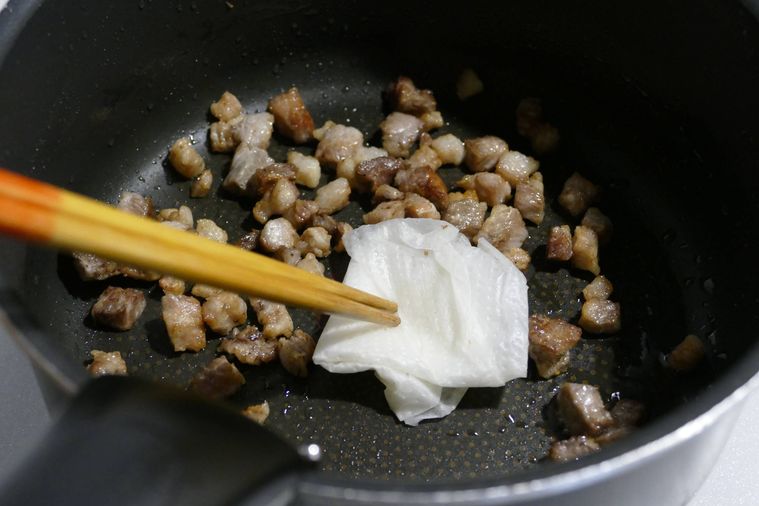 角切りの豚肉をフライパンで炒めながら出てきた脂を拭く様子