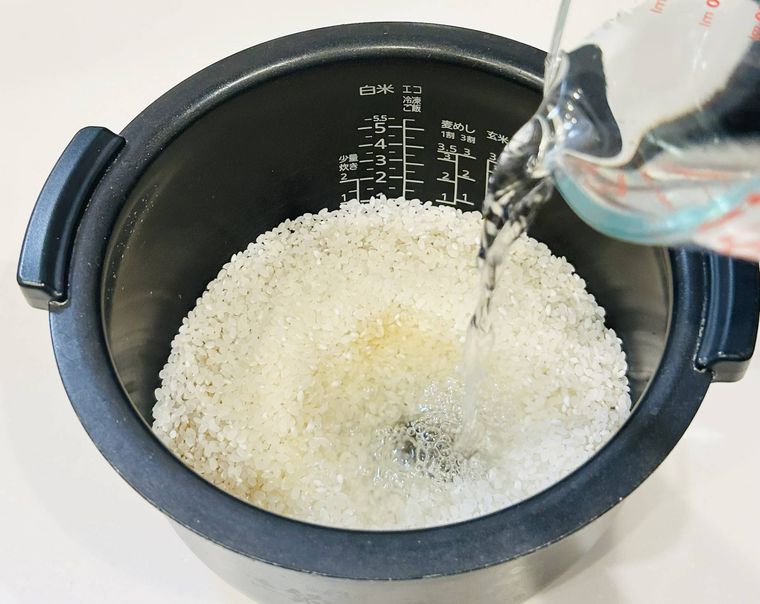 米と調味料が入った炊飯器に水を加えているところ