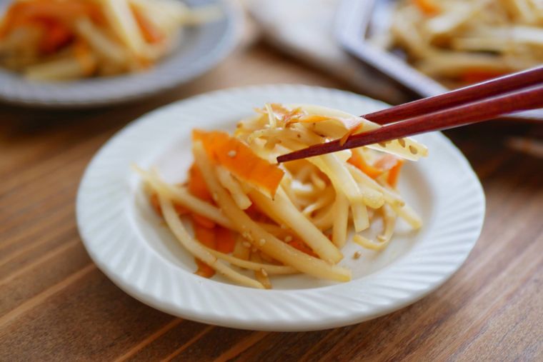 八角型の茶色い器に盛られたきんぴらに、いりごまをかける様子