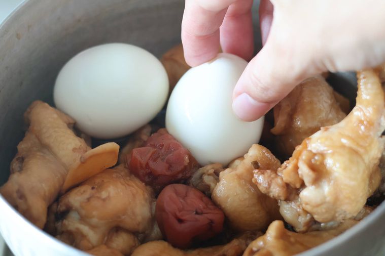 鶏肉の入った鍋にゆで卵を入れている