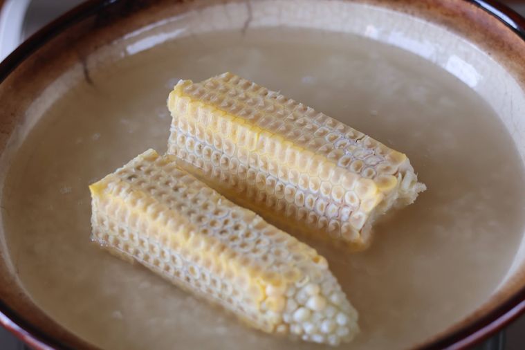 土鍋に入れた米とだしの上にとうもろこしの芯がのっている