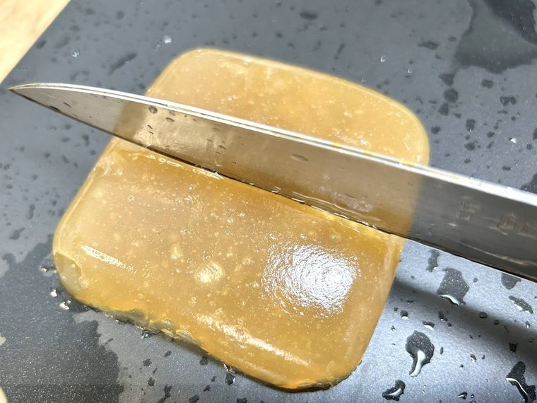 黒いまな板に置いたわらび餅を包丁で切っている様子