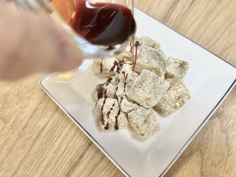 白い皿に盛り付けたわらび餅に黒蜜をかけている様子