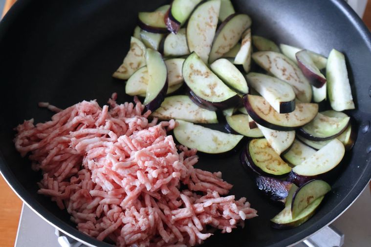 なすを炒めたフライパンにひき肉が入っている