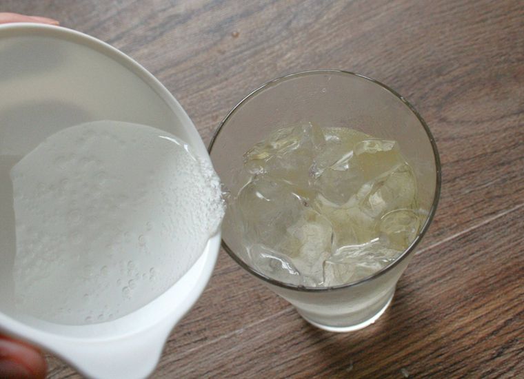 氷とウイスキーの入ったタンブラーグラスに炭酸水をそそいでいる様子