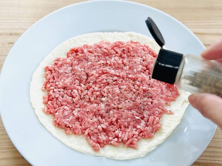 合い挽き肉をのせたトルティーヤに粗挽き黒こしょうを振っている様子