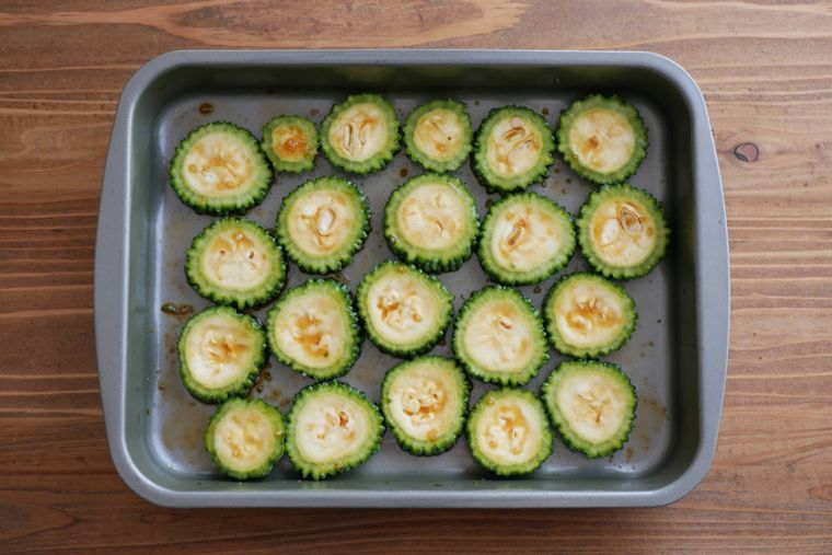 金属製バットの上でゴーヤの輪切りを調味料に漬けている様子