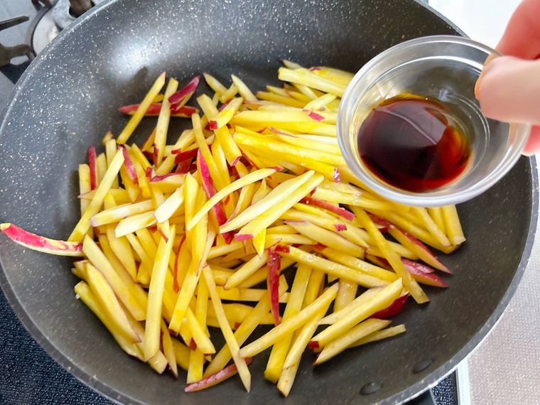 さつまいもを炒めているところにしょうゆを入れる様子