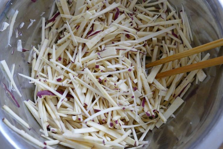 細切りさつまいもに塩を加えて箸で混ぜる様子