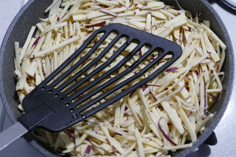 フライパンに広げた細切りさつまいもをフライ返しで押さえる様子