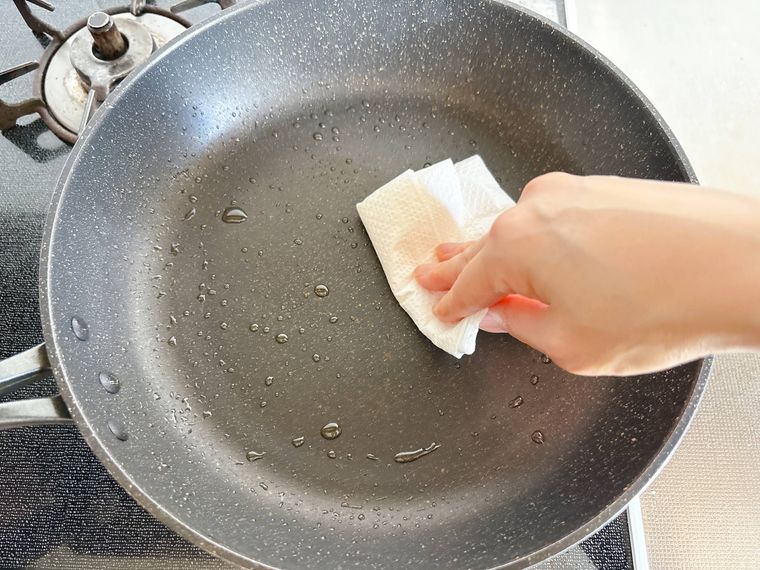 キッチンペーパーでフライパンの油を拭く様子