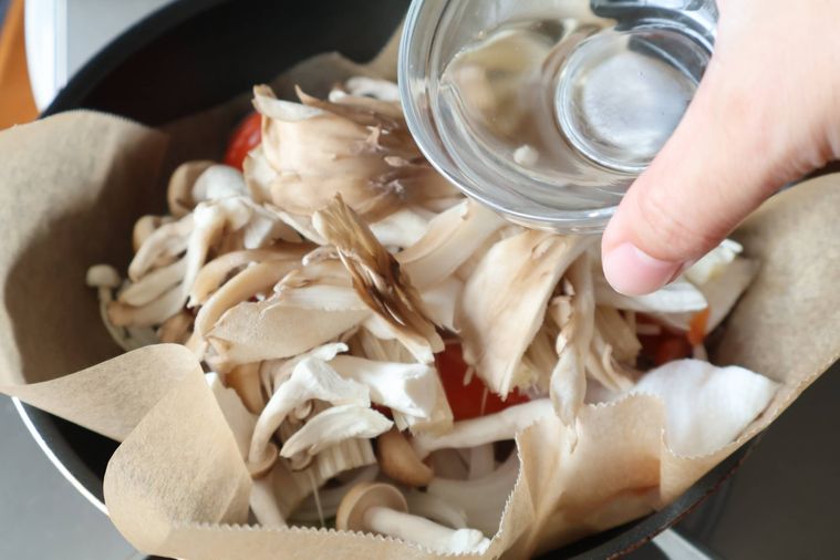 フライパンに入れた食材の上に酒をかけている