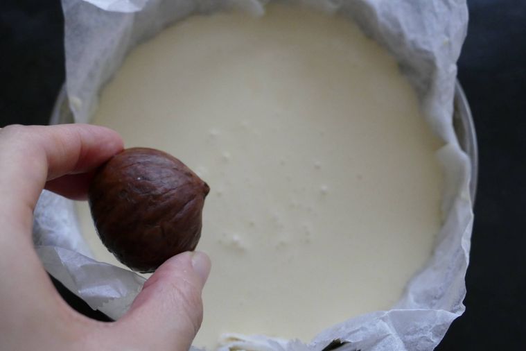 型に流し入れたチーズケーキに栗の渋皮煮を入れる様子