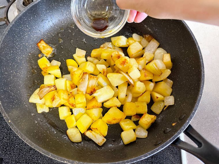フライパンの玉ねぎとじゃがいもにしょうゆをまわしかける様子
