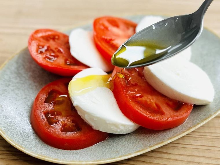 トマトとモッツァレラチーズにオリーブオイルをかけている様子