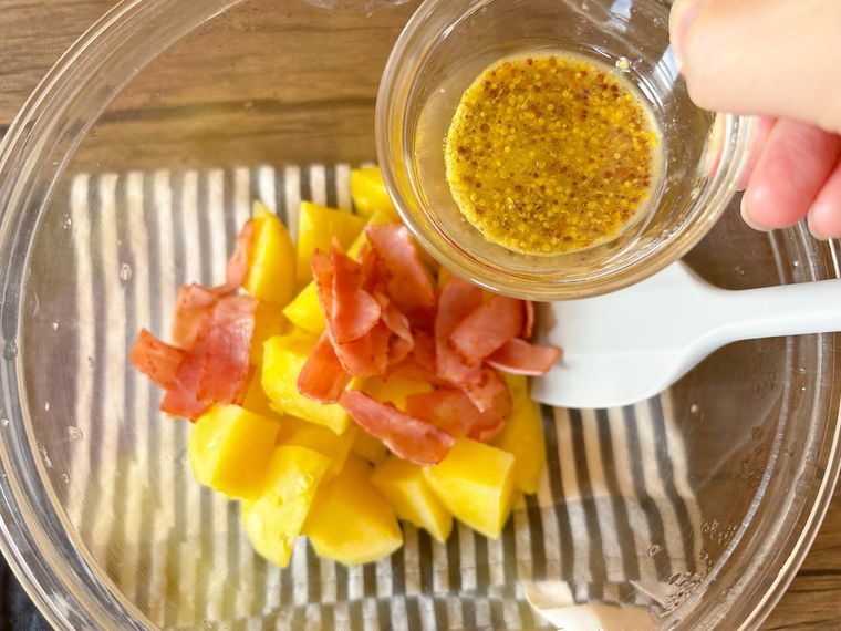 ボウルに入ったじゃがいもとベーコンにドレッシングを加える様子