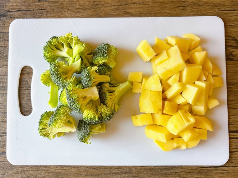 まな板におかれた小房に分けたブロッコリー、1cm角のじゃがいも