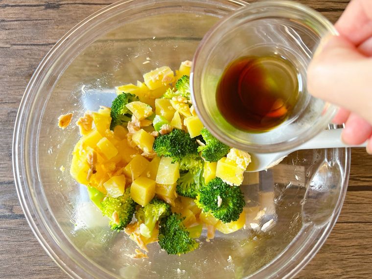 ブロッコリー、じゃがいもツナ缶が入ったボウルにしょうゆを加える様子