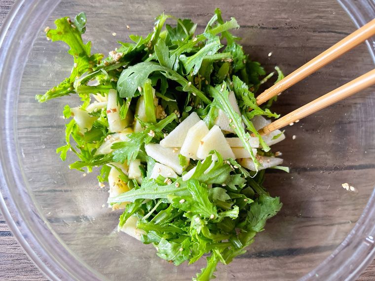 ボウルで春菊、りんご、ドレッシングを和える様子