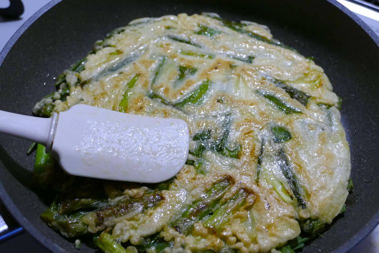 チヂミの表面をヘラで押さえながら焼く様子