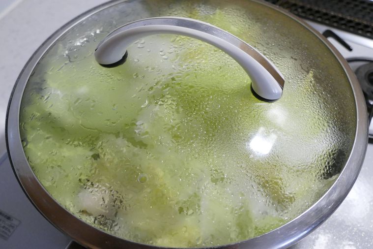 白菜の葉と調味料を入れて蓋をして蒸し煮にする様子