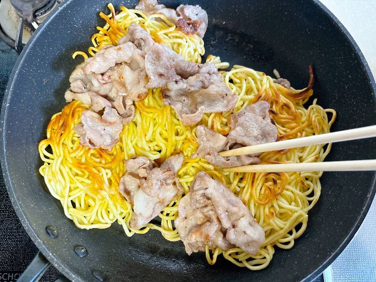 フライパンで中華麺、豚こま肉を炒める様子