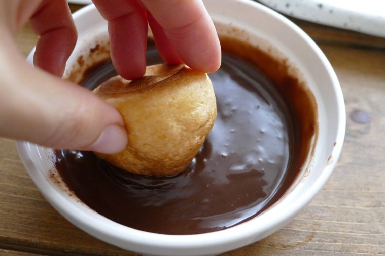 プチシュークリームを手で持ってチョコレートソースにディップする様子