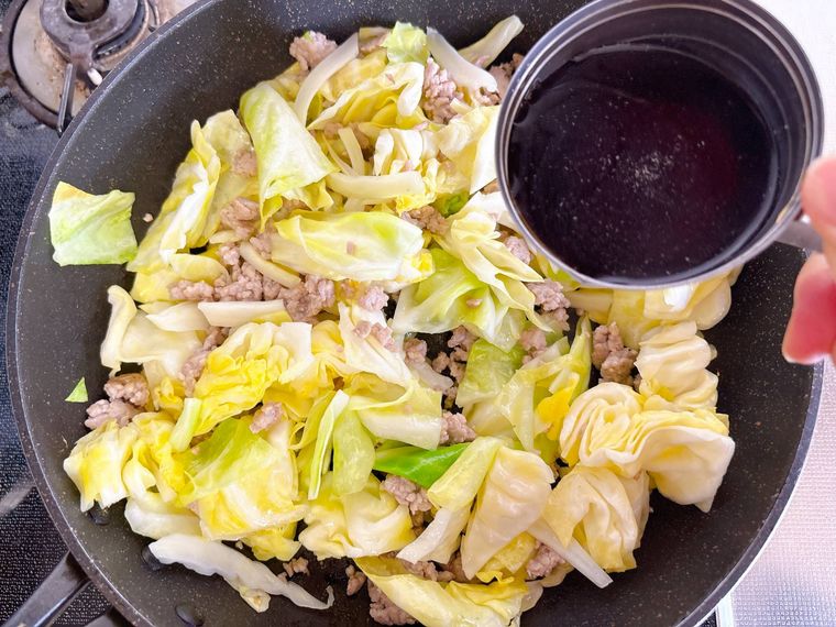 キャベツと豚ひき肉の炒めたものに調味料を加える様子