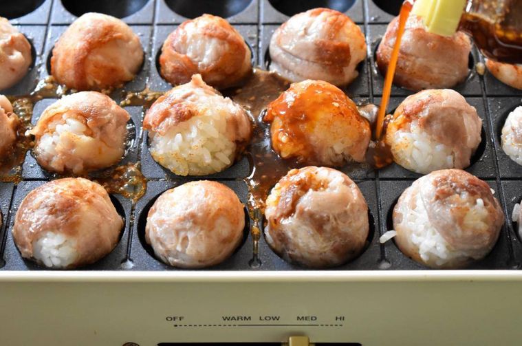 たこ焼き器の中でたれをかけた肉巻きおにぎり