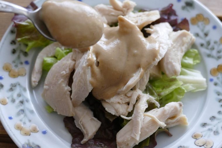 サラダチキンとレタスにごまドレッシングをかける様子