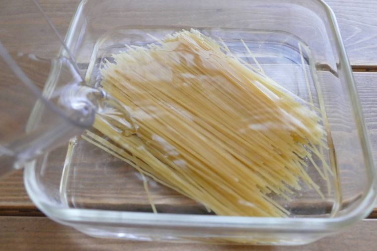 スパゲッティと塩が入っている容器に水を入れる様子