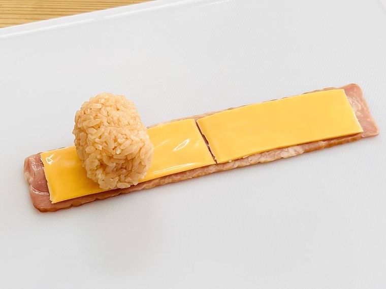 チーズを並べたベーコンの上に俵型のおにぎりをのせた様子