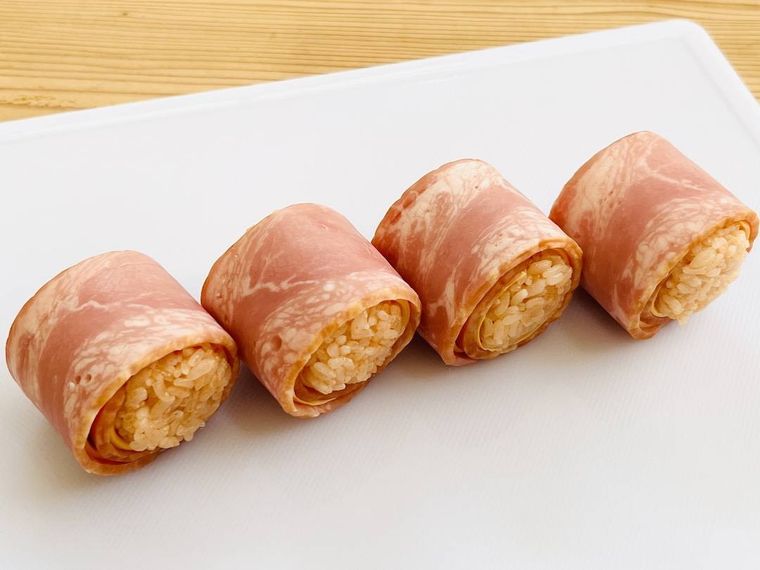 俵型のおにぎりをチーズとベーコンで巻いた様子