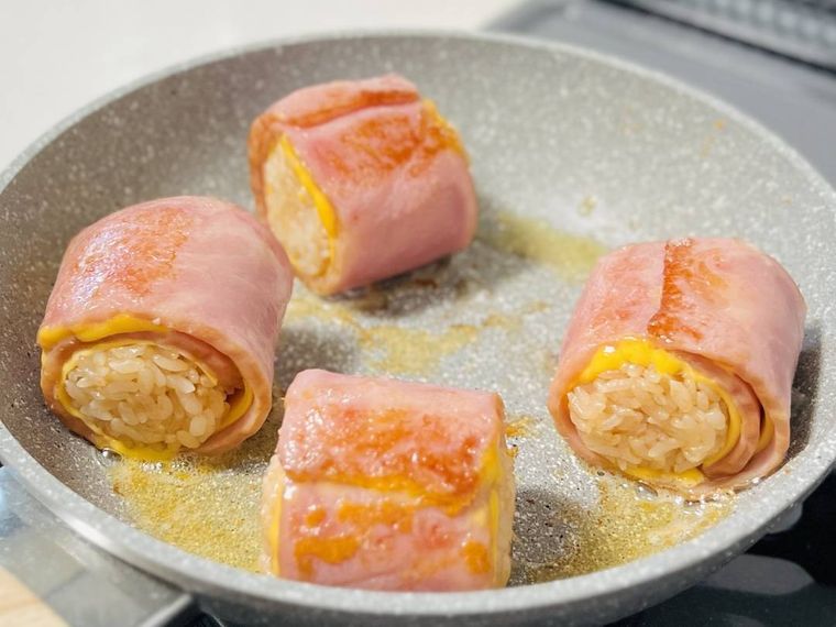 チーズとベーコンで巻いたおにぎりをフライパンで焼いている様子