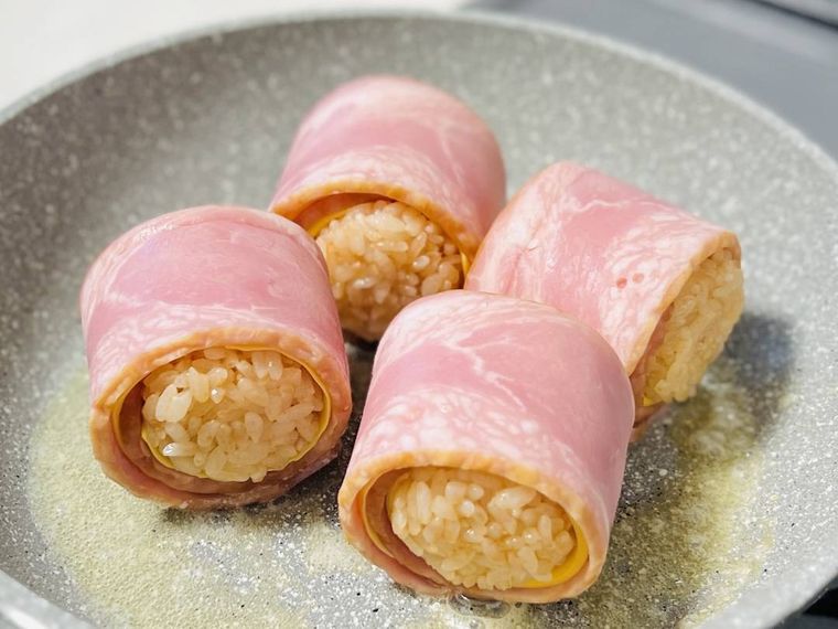 チーズとベーコンで巻いたおにぎりをフライパンで焼いている様子