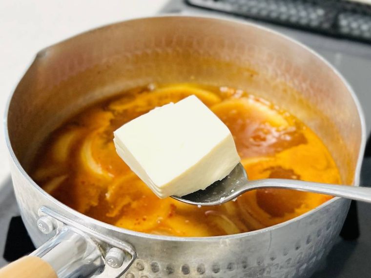 玉ねぎ入りのコチュジャンスープに豆腐を加えている様子