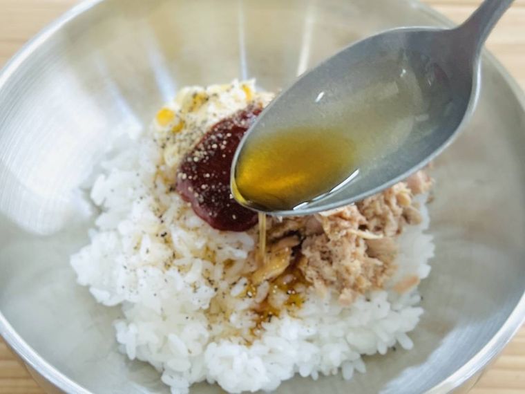 ツナ缶、マヨネーズ、コチュジャンをのせたごはんに、粗挽き黒こしょうとごま油をかけている様子