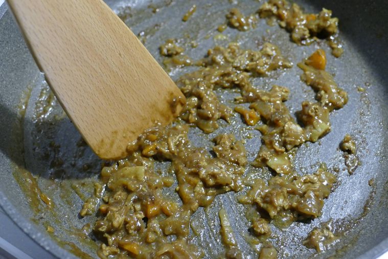 ヘラでカレーの具材を潰しながら炒める様子
