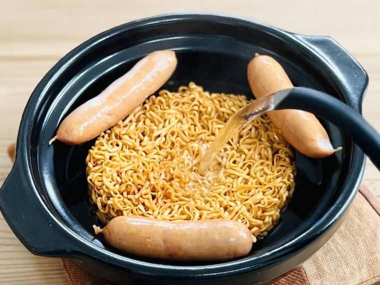 チキンラーメンとウインナーが入った土鍋に熱湯をそそいでいる様子
