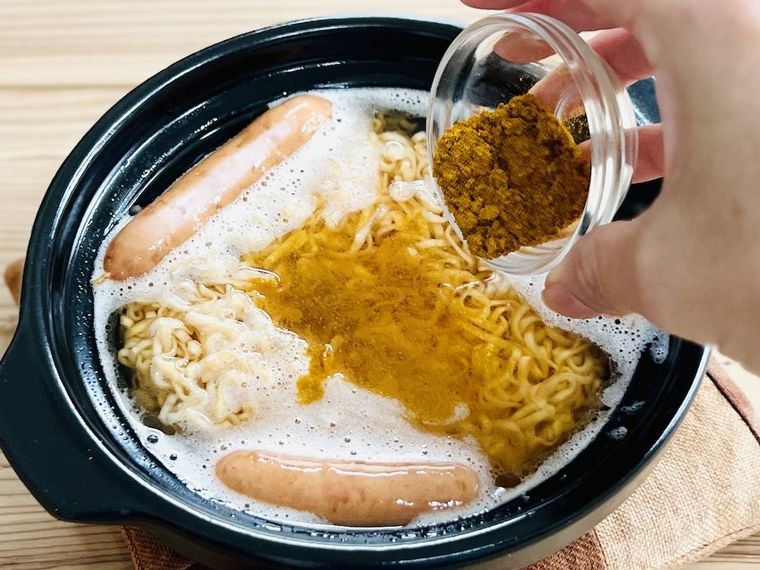 チキンラーメン、ウインナー、お湯が入った土鍋にカレー粉を加えている様子