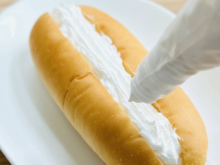 ホットドッグパンの切り込みにホイップクリームを絞っている様子