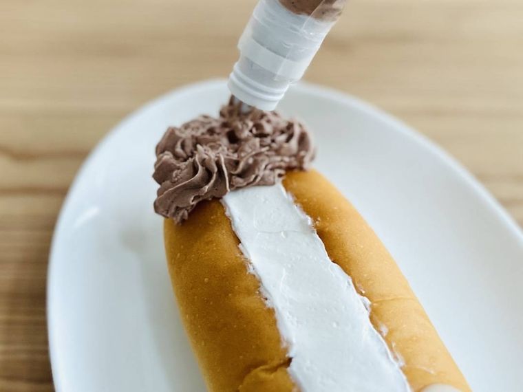 ホットドッグパンの上部にチョコレートホイップクリームを絞っている様子